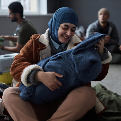 Front view portrait of young Middle Eastern woman playing with baby sitting on floor at refugee shelter, copy space